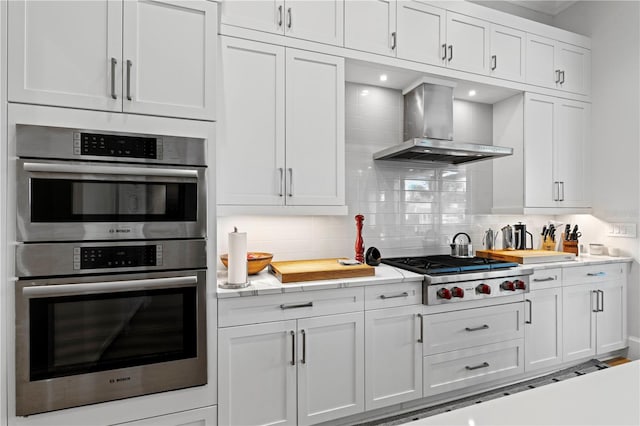 kitchen featuring backsplash, stainless steel appliances, white cabinets, and wall chimney range hood