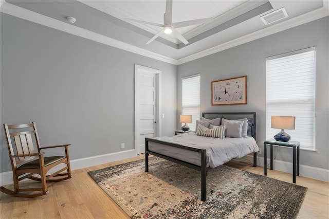 bedroom with crown molding, a raised ceiling, light hardwood / wood-style flooring, and ceiling fan