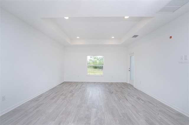 empty room featuring a tray ceiling and light hardwood / wood-style flooring