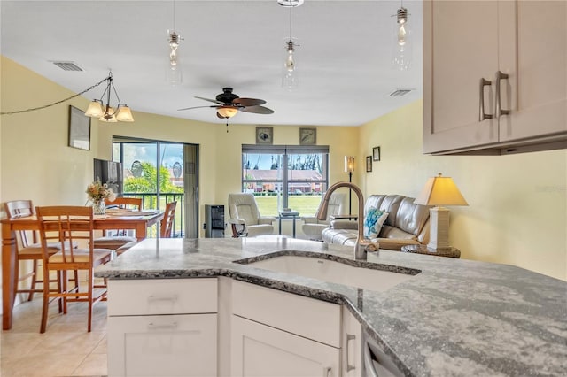 kitchen with stone counters, sink, white cabinets, hanging light fixtures, and light tile patterned floors