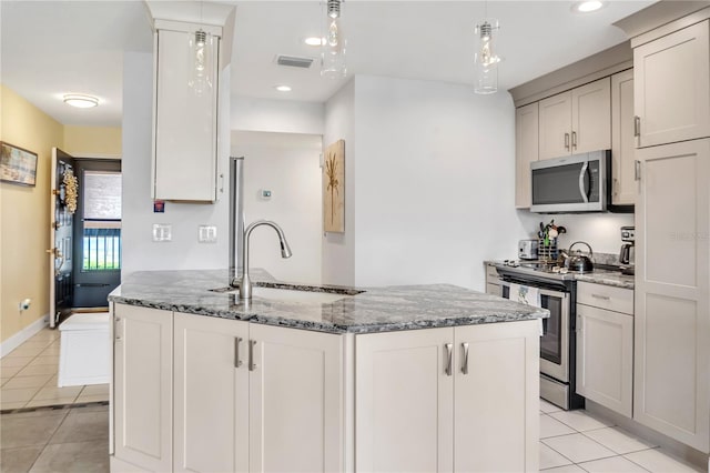 kitchen with sink, light tile patterned floors, stainless steel appliances, decorative light fixtures, and dark stone counters