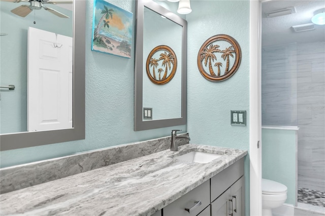 bathroom featuring vanity, ceiling fan, toilet, and tiled shower