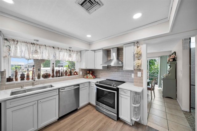 kitchen with plenty of natural light, stainless steel appliances, light wood-type flooring, and wall chimney range hood