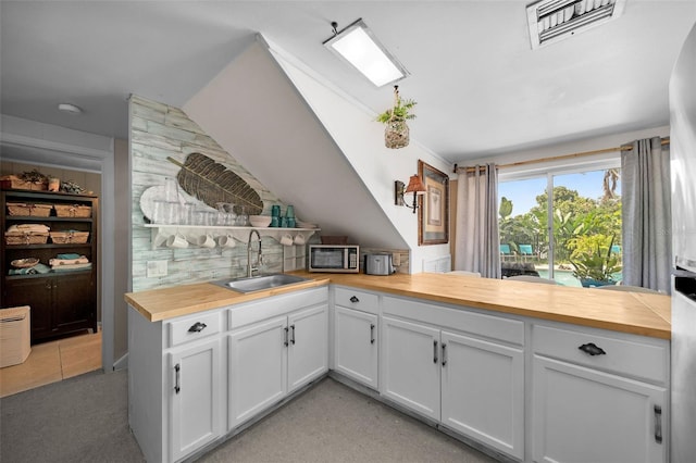 kitchen featuring white cabinets, vaulted ceiling, wood counters, and sink