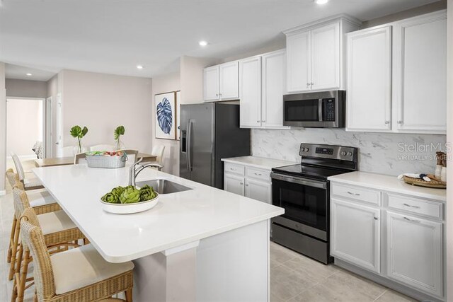 kitchen featuring a kitchen breakfast bar, backsplash, a kitchen island with sink, stainless steel appliances, and white cabinetry