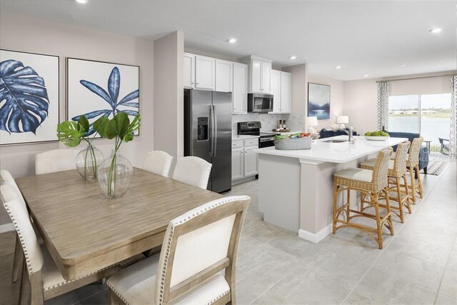 kitchen with white cabinets, stainless steel appliances, a center island with sink, and a breakfast bar