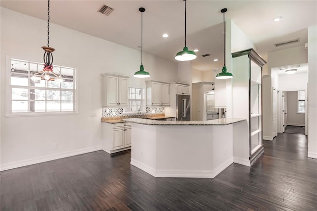 kitchen featuring dark wood-type flooring, white cabinetry, decorative backsplash, light stone countertops, and stainless steel fridge