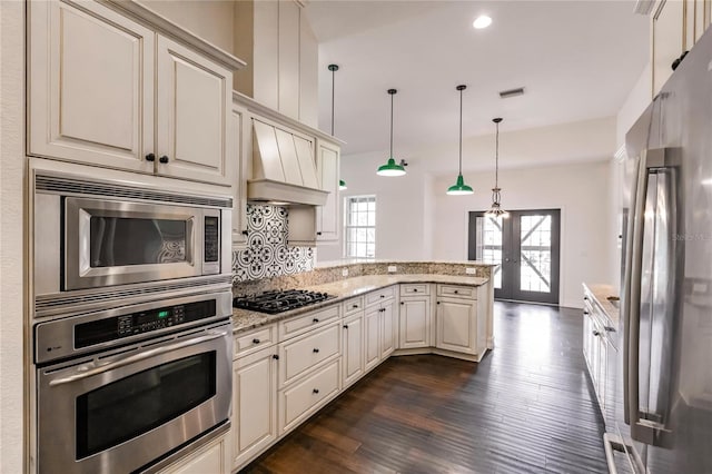 kitchen featuring premium range hood, decorative light fixtures, dark wood-type flooring, appliances with stainless steel finishes, and light stone countertops