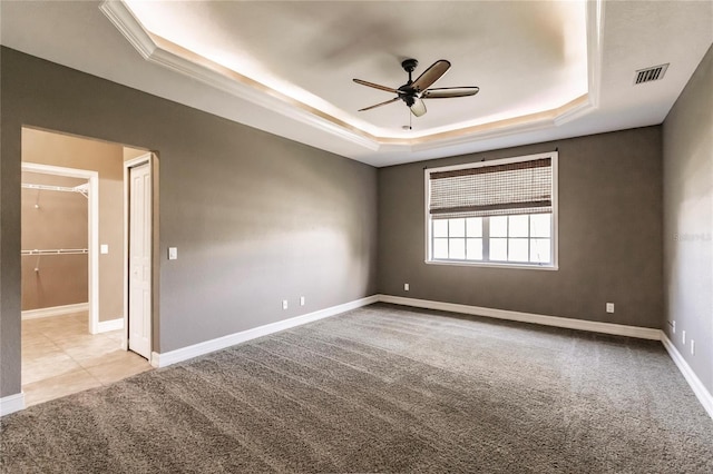 empty room with a raised ceiling, ceiling fan, and light carpet