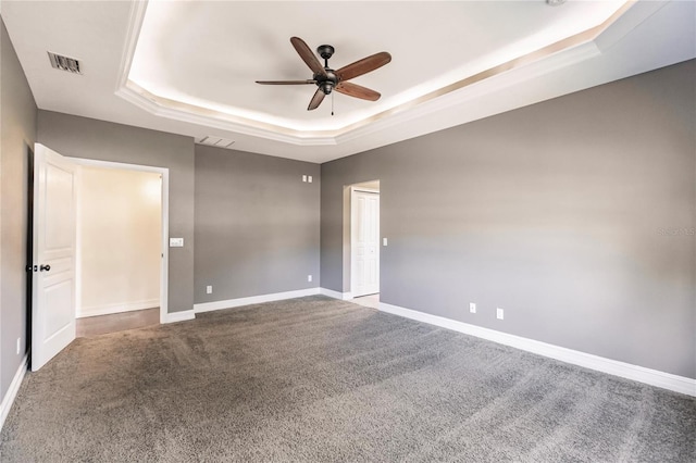 empty room with a tray ceiling, ceiling fan, and carpet flooring