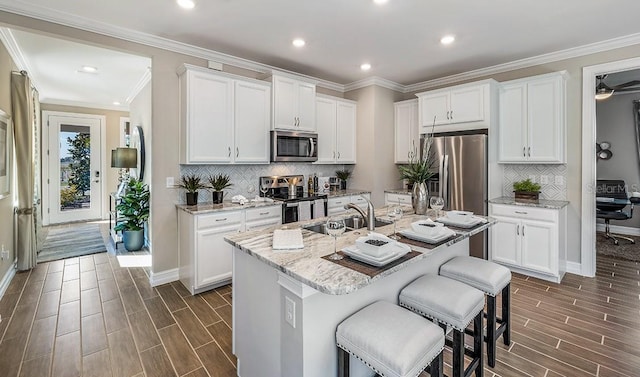 kitchen featuring decorative backsplash, appliances with stainless steel finishes, a kitchen island with sink, sink, and white cabinets