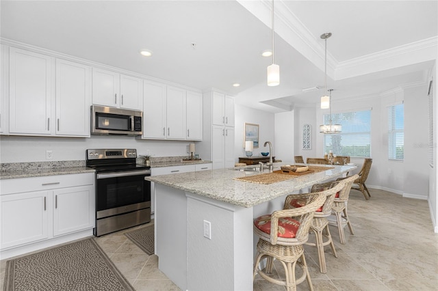 kitchen featuring decorative light fixtures, stainless steel appliances, white cabinetry, sink, and a center island with sink