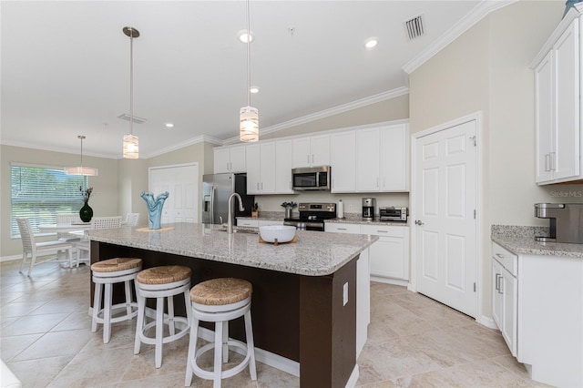 kitchen featuring white cabinets, stainless steel appliances, lofted ceiling, decorative light fixtures, and a center island with sink