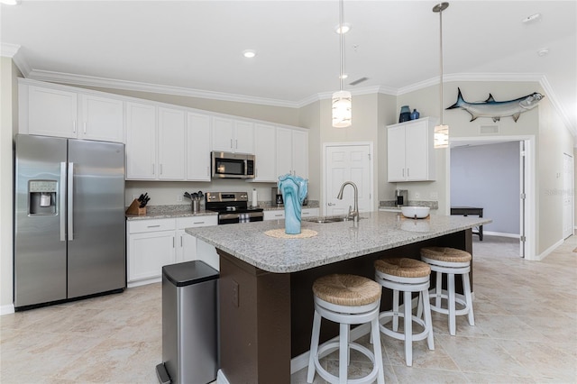 kitchen with light stone counters, hanging light fixtures, a kitchen island with sink, white cabinetry, and stainless steel appliances