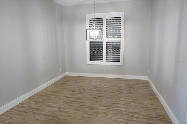 empty room with a notable chandelier and light hardwood / wood-style floors