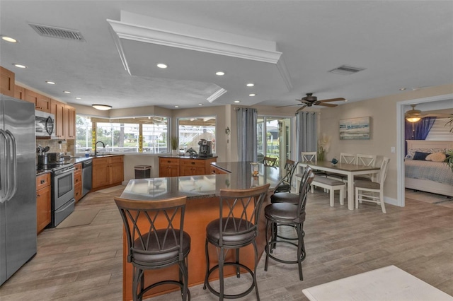 kitchen featuring appliances with stainless steel finishes, light hardwood / wood-style floors, sink, ceiling fan, and a breakfast bar