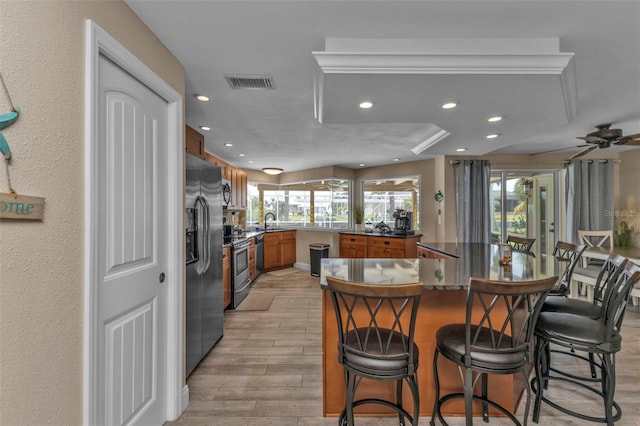 kitchen with light wood-type flooring, stainless steel appliances, kitchen peninsula, ceiling fan, and a breakfast bar