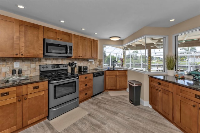 kitchen with light hardwood / wood-style flooring, backsplash, appliances with stainless steel finishes, sink, and dark stone counters