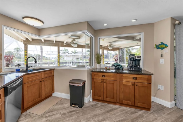 kitchen with stainless steel dishwasher, sink, light wood-type flooring, and dark stone counters