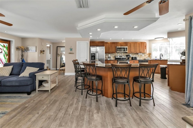 kitchen featuring a center island, ceiling fan, appliances with stainless steel finishes, a breakfast bar area, and light hardwood / wood-style floors