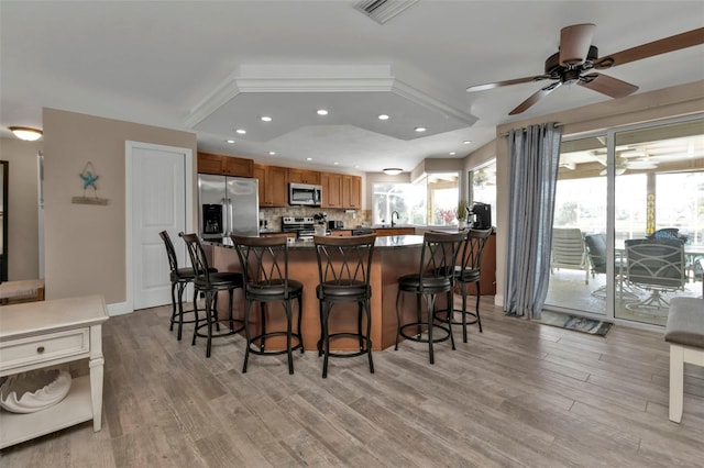 kitchen with backsplash, appliances with stainless steel finishes, light hardwood / wood-style floors, sink, and ceiling fan