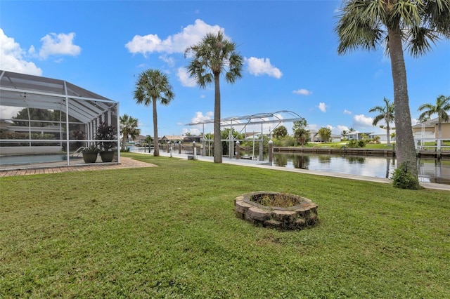 view of yard featuring glass enclosure, a dock, a water view, and a fire pit