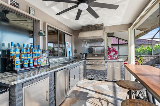 kitchen with wall chimney range hood, stainless steel refrigerator, ceiling fan, and stone countertops