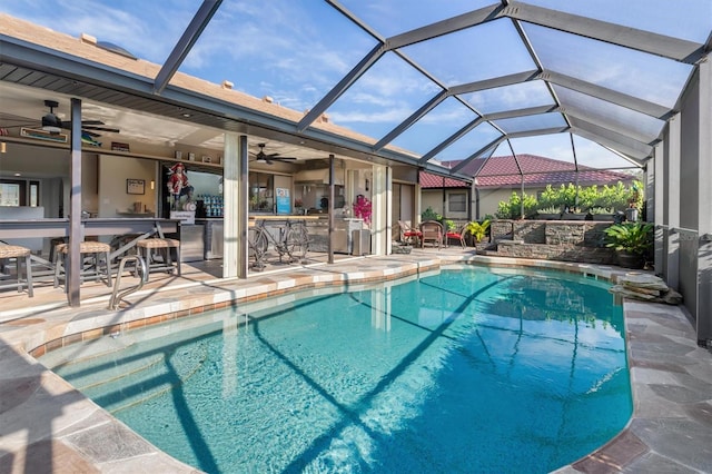 view of pool with glass enclosure, ceiling fan, a bar, and a patio