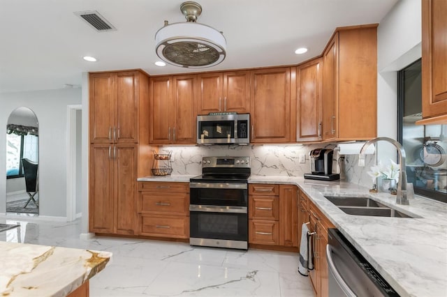 kitchen featuring light stone countertops, backsplash, stainless steel appliances, and sink