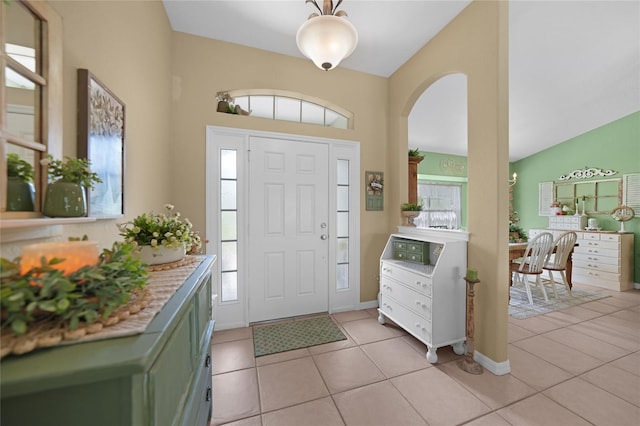 foyer featuring light tile patterned floors, arched walkways, baseboards, and vaulted ceiling