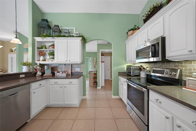 kitchen featuring arched walkways, open shelves, dark countertops, and appliances with stainless steel finishes