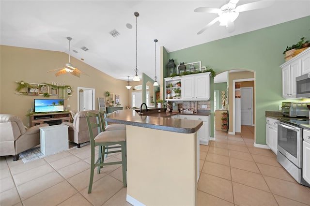 kitchen with stainless steel appliances, dark countertops, a ceiling fan, arched walkways, and open floor plan