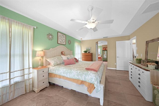bedroom featuring a ceiling fan, arched walkways, a tray ceiling, and visible vents
