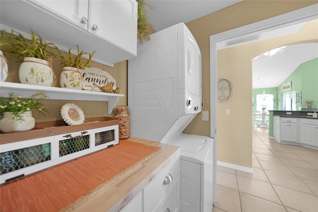 laundry area with cabinets, stacked washer / drying machine, and light tile patterned floors