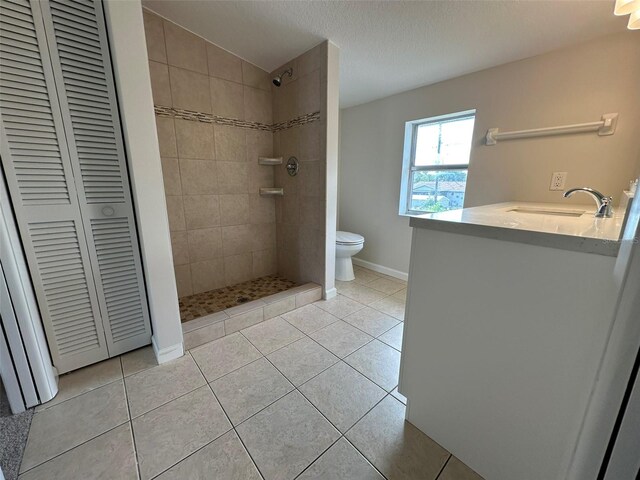 bathroom with vanity, tile patterned flooring, toilet, a textured ceiling, and a tile shower