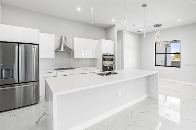 kitchen with decorative light fixtures, appliances with stainless steel finishes, white cabinetry, wall chimney exhaust hood, and an island with sink