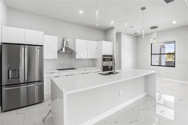 kitchen featuring white cabinetry, decorative light fixtures, stainless steel appliances, an island with sink, and wall chimney range hood