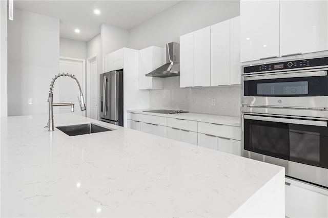 kitchen with stainless steel appliances, light stone counters, sink, and wall chimney range hood