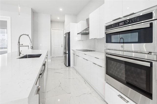 kitchen featuring stainless steel appliances, sink, hanging light fixtures, wall chimney exhaust hood, and white cabinets