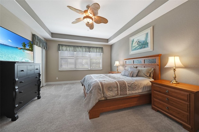 bedroom with light carpet, ceiling fan, and a tray ceiling