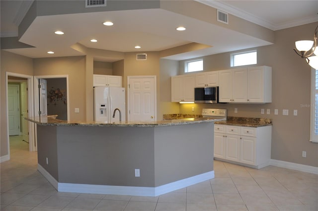 kitchen featuring ornamental molding, dark stone counters, white refrigerator with ice dispenser, a kitchen island with sink, and white cabinets