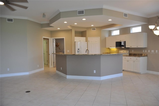 kitchen featuring light stone counters, ornamental molding, a center island with sink, white refrigerator with ice dispenser, and white cabinetry