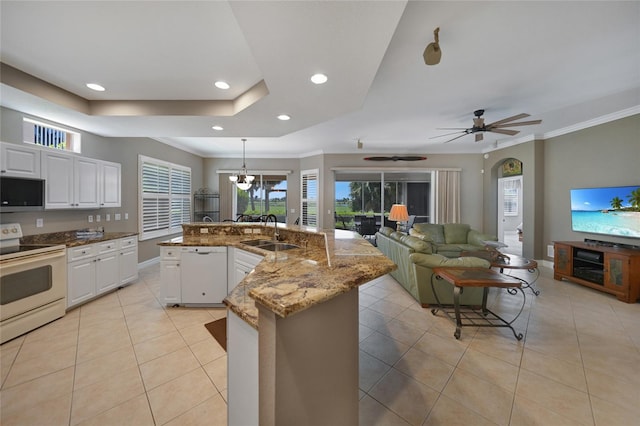 kitchen featuring ceiling fan with notable chandelier, white cabinets, hanging light fixtures, a kitchen island with sink, and white appliances