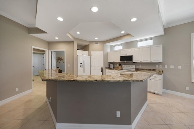 kitchen featuring dark stone countertops, white cabinetry, white appliances, and a large island with sink