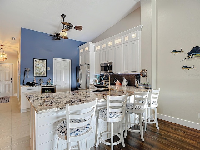 kitchen with white cabinets, lofted ceiling, kitchen peninsula, appliances with stainless steel finishes, and ceiling fan