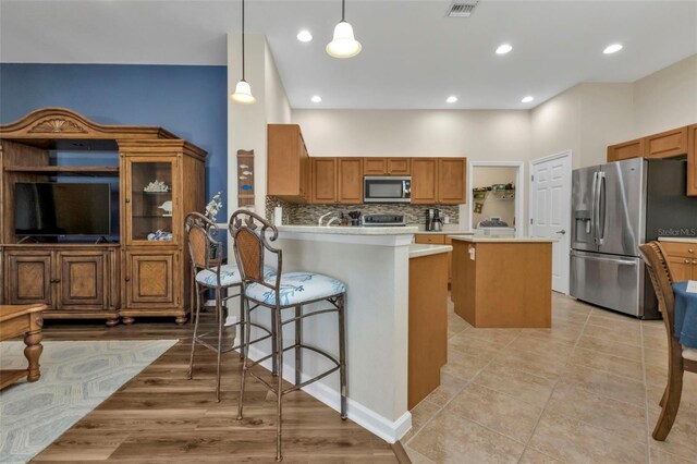 kitchen featuring decorative backsplash, kitchen peninsula, a breakfast bar, stainless steel appliances, and decorative light fixtures