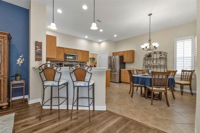 kitchen with kitchen peninsula, appliances with stainless steel finishes, light hardwood / wood-style flooring, an inviting chandelier, and a breakfast bar area