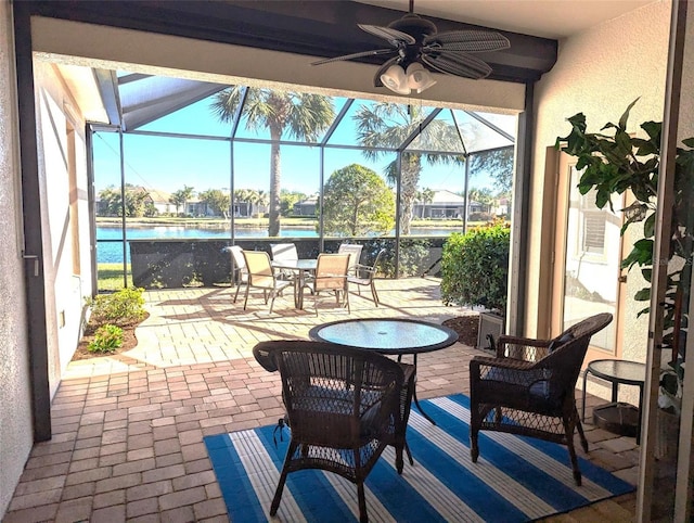 view of patio / terrace featuring glass enclosure, ceiling fan, and a water view