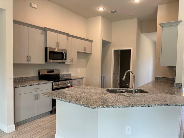 kitchen with kitchen peninsula, light stone countertops, stainless steel appliances, sink, and light hardwood / wood-style flooring