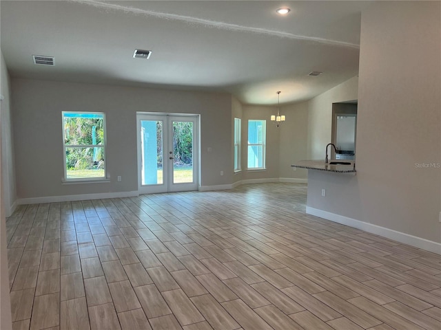 unfurnished room featuring an inviting chandelier, french doors, sink, and light hardwood / wood-style flooring